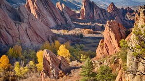 Un paisaje montañoso con formaciones rocosas rojas prominentes y árboles de colores otoñales.