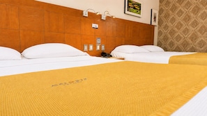 Habitación de hotel con dos camas, cabecero de madera, colcha amarilla y lámpara fijada a la pared.