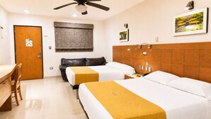 Habitación de hotel con dos camas, un escritorio, una silla, ventilador de techo, ventana con persianas, cabecera de madera y un cuadro en la pared.