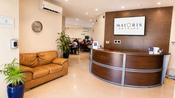 Una recepción de hotel con un reloj, un sofá de cuero marrón y plantas en macetas.