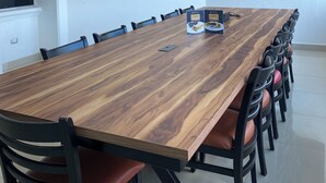 Un salón de conferencias con una larga mesa de madera, sillas negras con asientos de cuero, un televisor de pantalla plana montado en la pared y dos letreros en la pared.