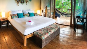 Un dormitorio amplio con una cama grande, un banco de madera y vistas a exuberante vegetación a través de un ventanal.
