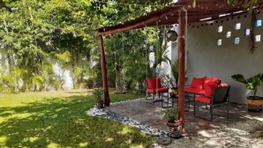 Un espace extérieur abrité, aménagé avec des chaises rouges, une balançoire et un pot de fleurs.