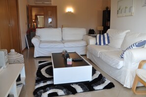 A living room with a white sofa set, a black and white rug, a coffee table, and a bookshelf.