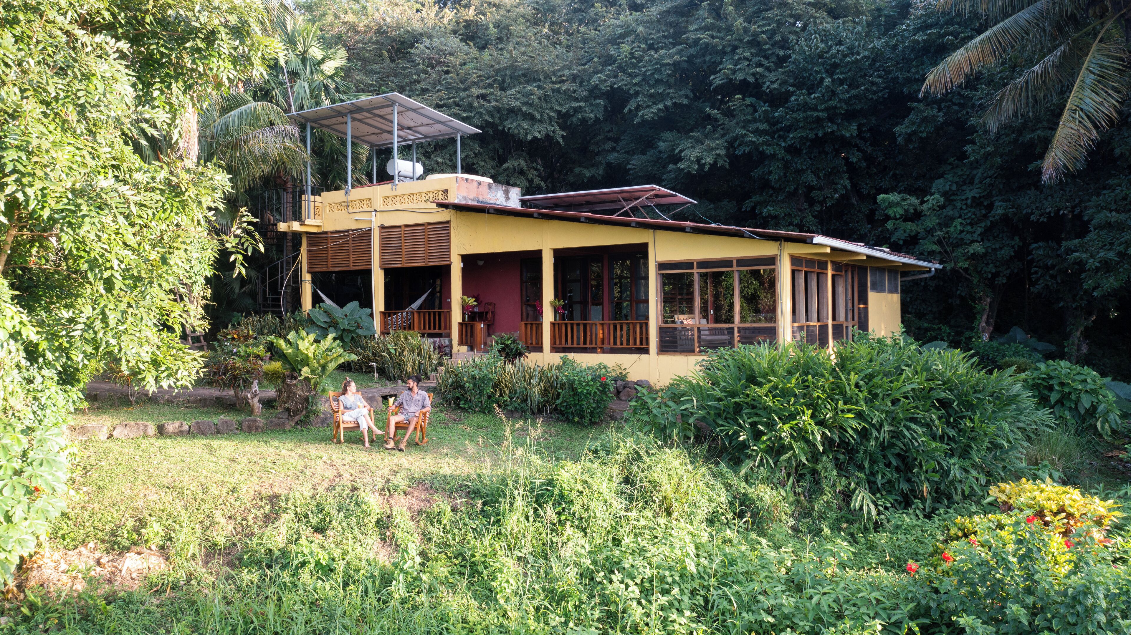 A two-story house with a covered porch, surrounded by lush greenery and a garden.