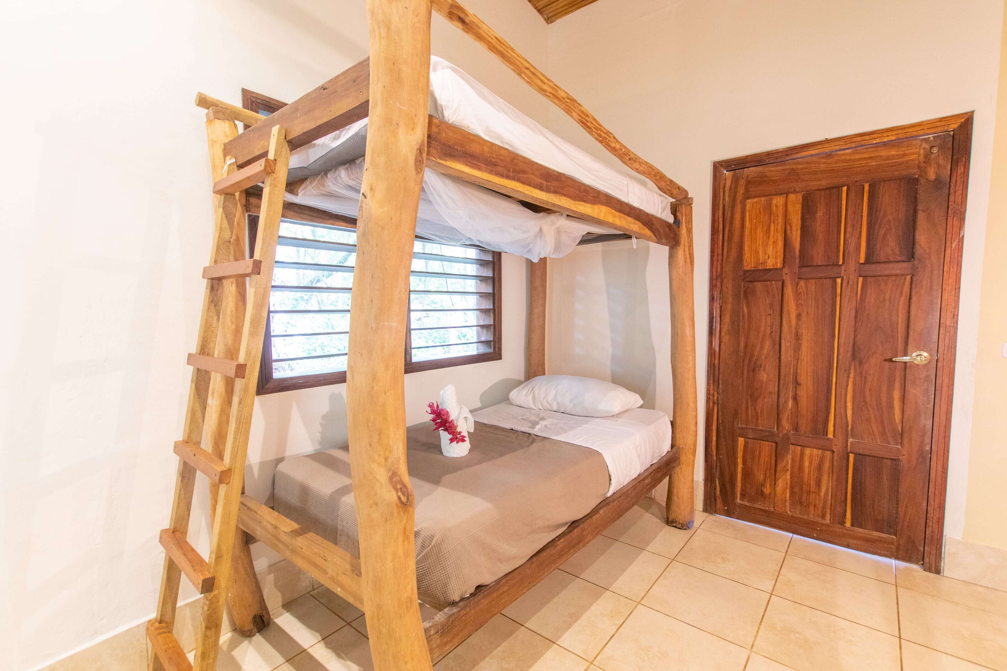 Una cama litera de madera con una escalera, una ventana con persianas, una puerta de madera y un suelo de baldosas.