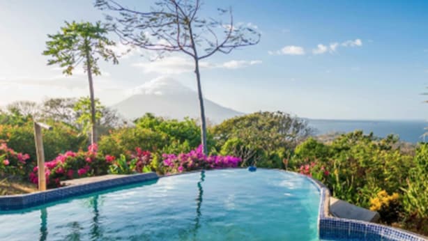 A clear view of a swimming pool with a tiled edge, surrounded by lush greenery and a mountain in the background. - Totoco Eco Resort (Altagracia)