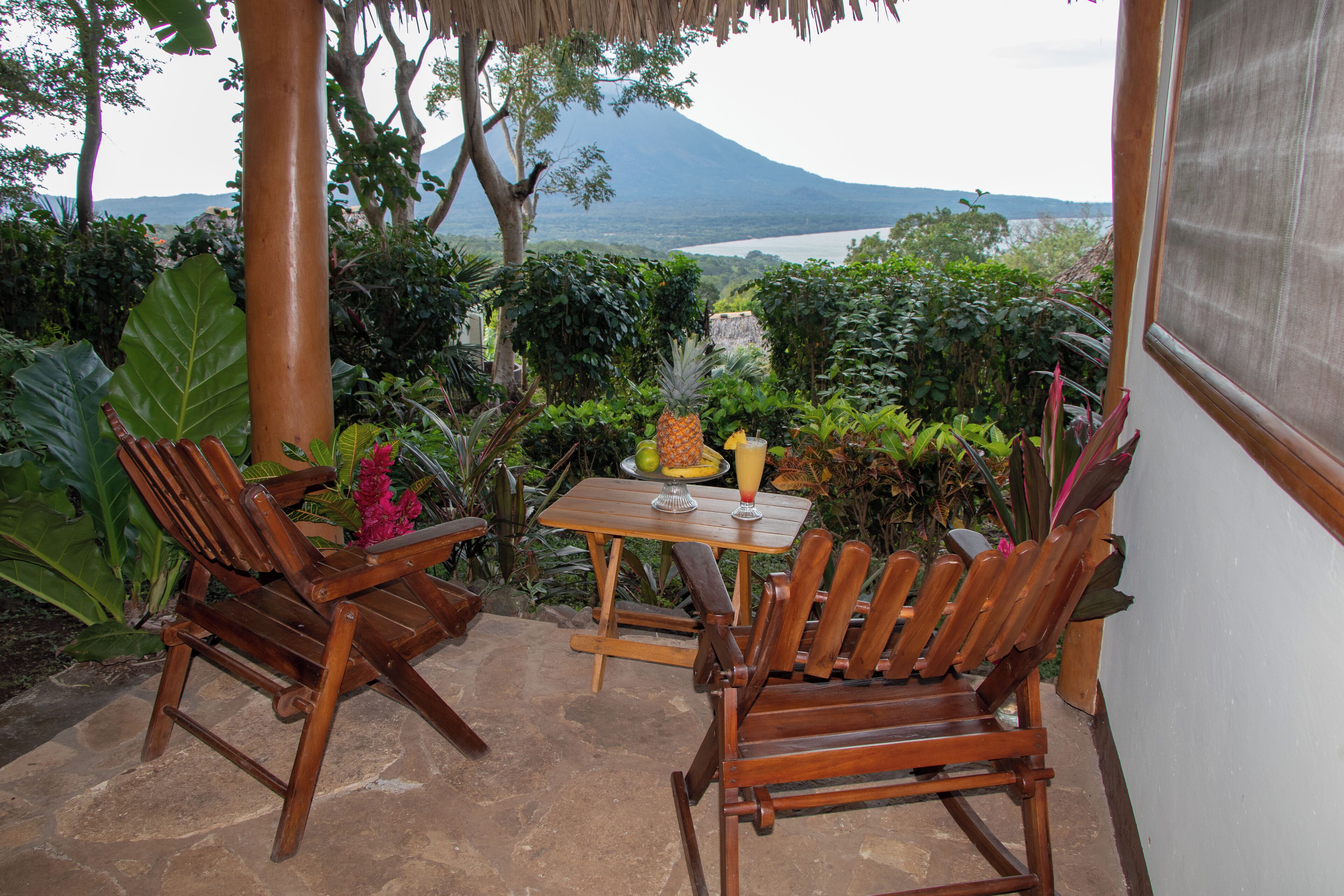 Ein Holztisch und zwei Stühle auf einer Terrasse mit Blick auf einen Berg und einen See.