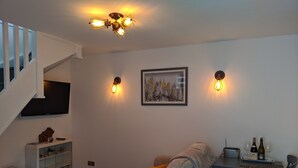 Una sala de estar con un sofá, una mesa de centro, un televisor, una estantería y una escalera.