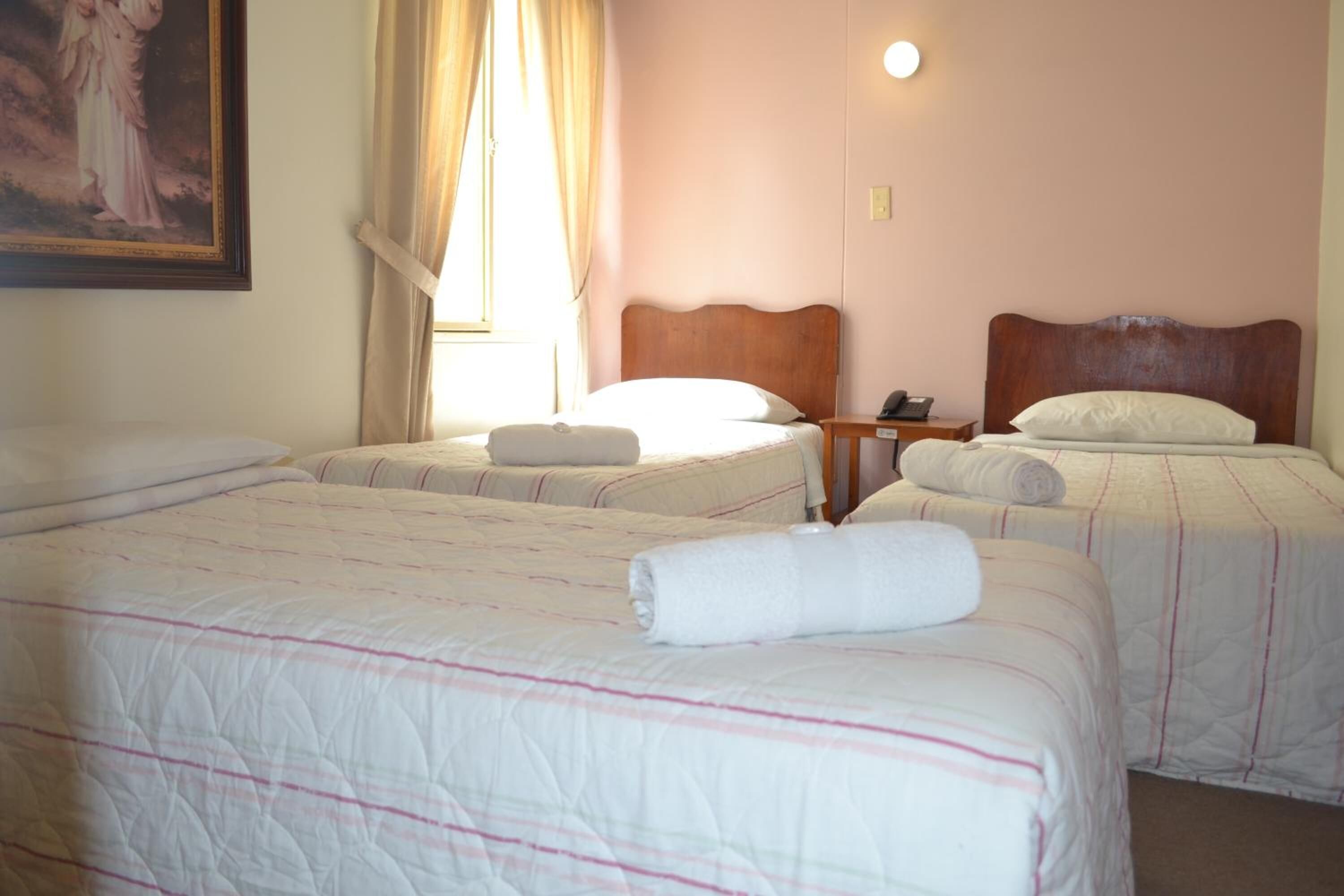 Habitación de hotel con dos camas, cada una con cabecero de madera, mesita de noche con lámpara y un cuadro en la pared.