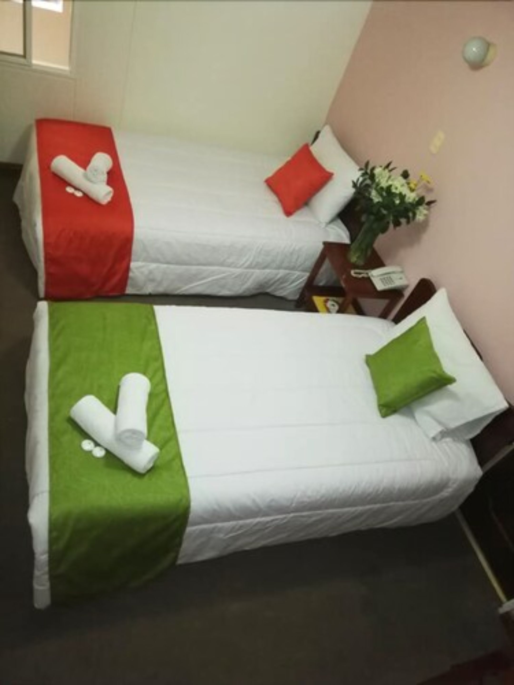 Two single beds with white bedding and red and green pillows.