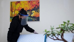 A person in a black uniform cleaning a bed with a blue quilted mattress and pillows. - Hotel Valle de Pubenza (Popayán)