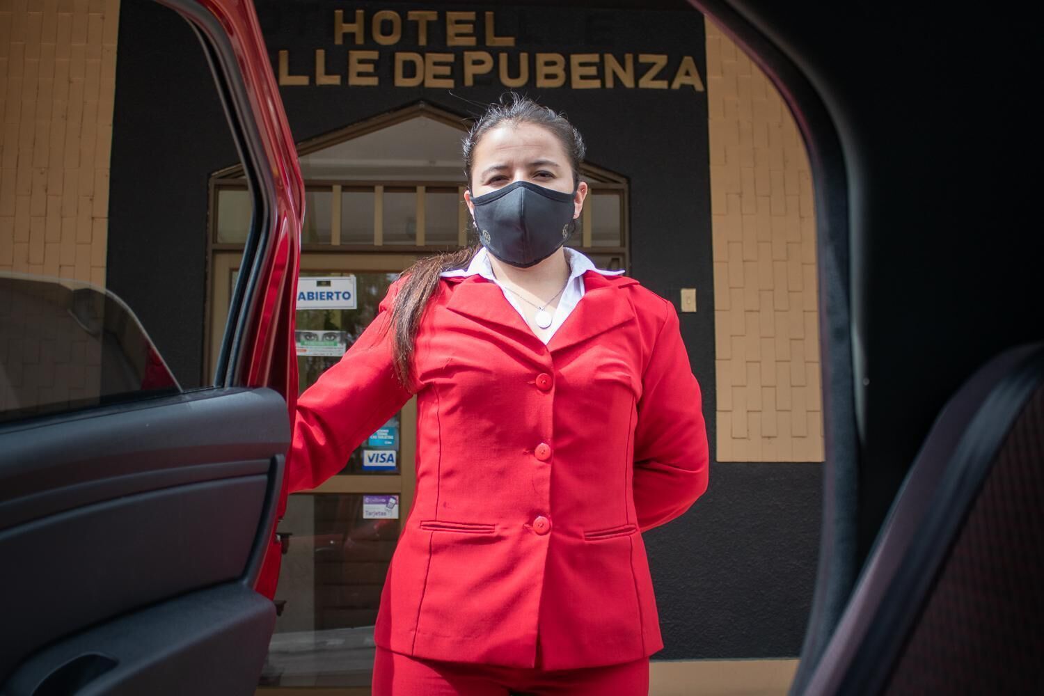 A person in a red uniform standing at the entrance of a building with a sign that reads "HOTEL LLE DEPUBENZA".