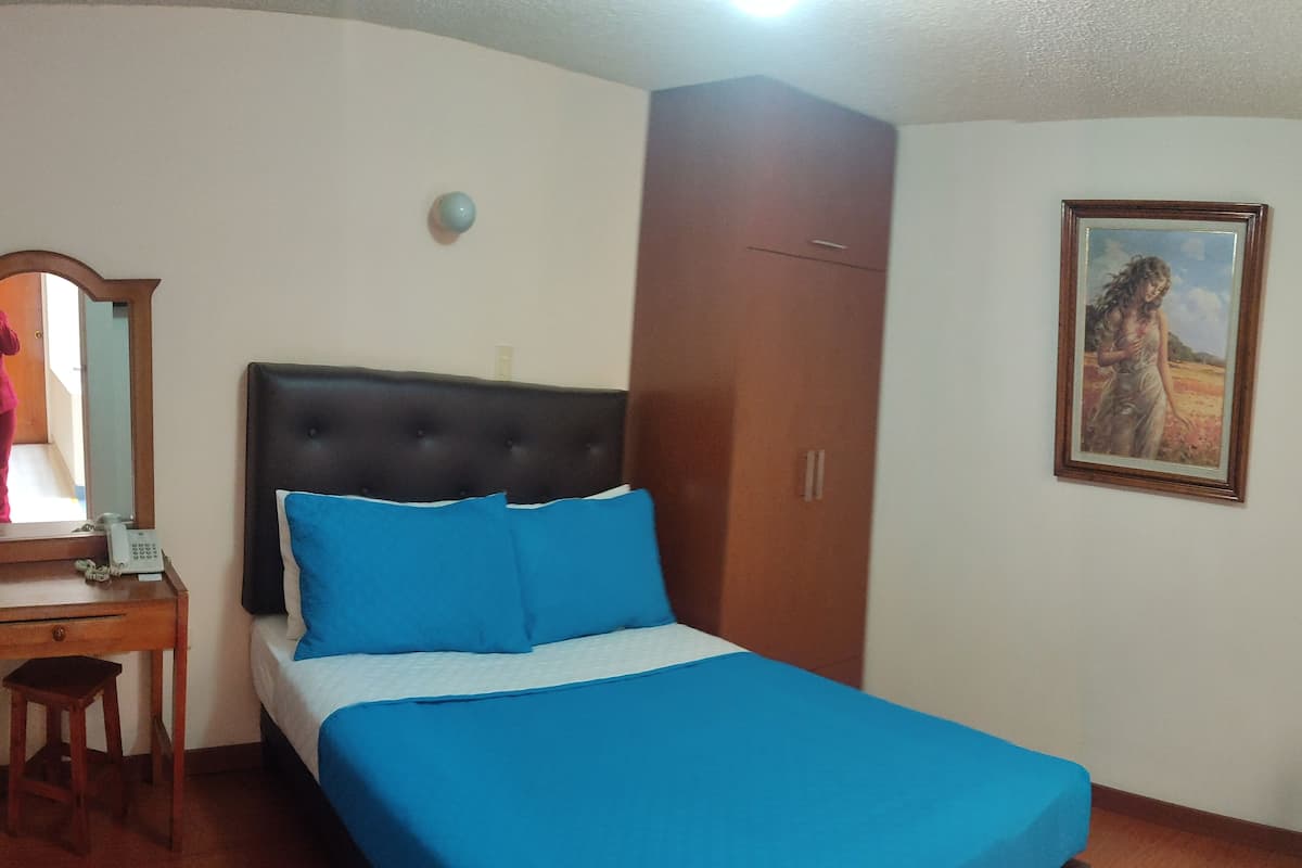 Un dormitorio con cama, mesita de noche, escritorio, silla, armario y un cuadro en la pared.