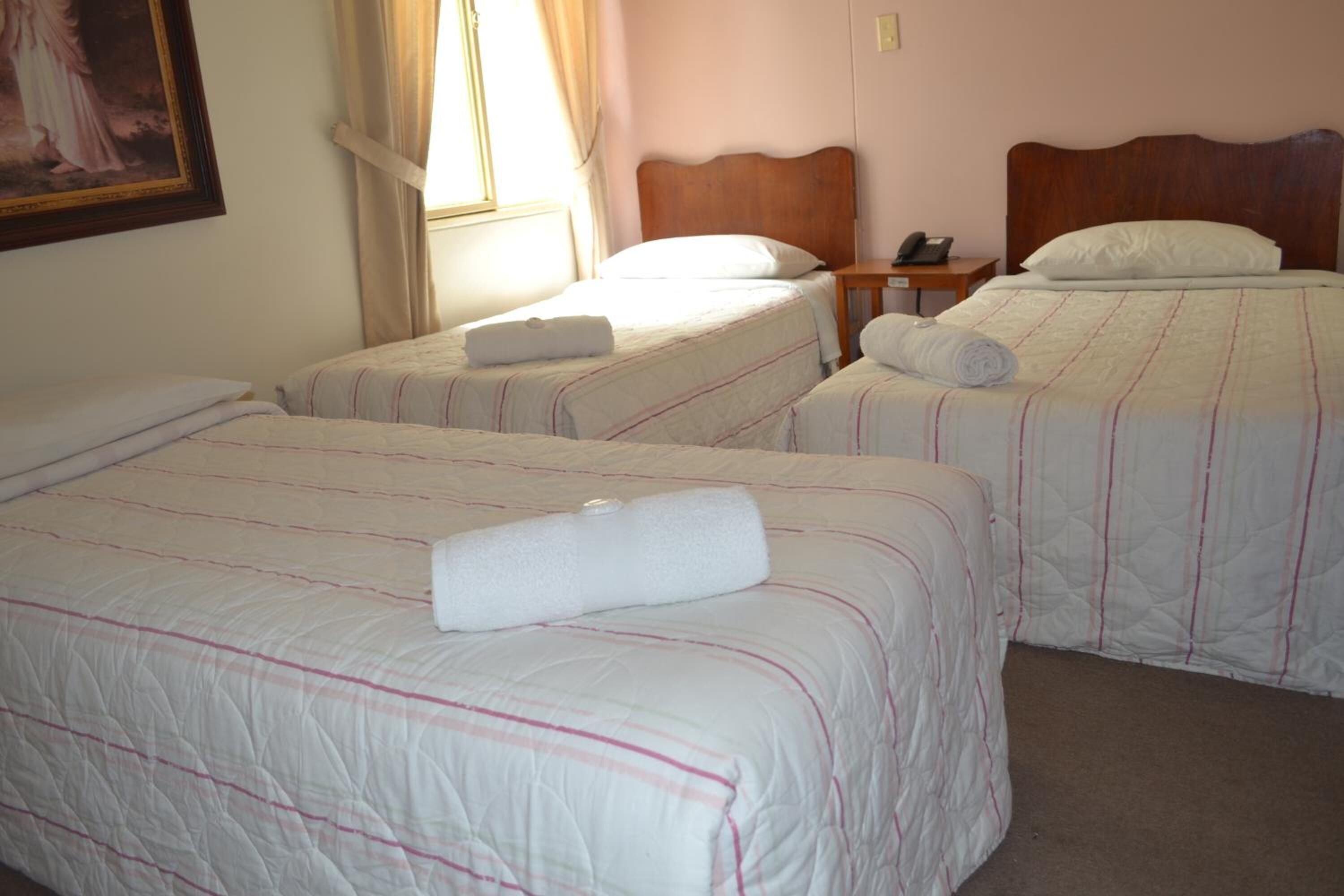 A hotel room with two single beds, each with a rolled white towel and a wooden headboard.