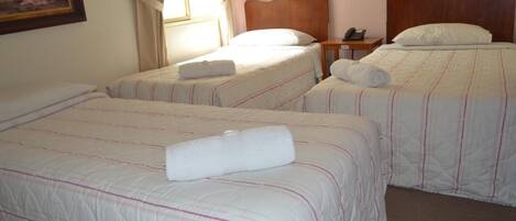 Habitación de hotel con dos camas individuales, cada una con una toalla blanca enrollada y un cabecero de madera.