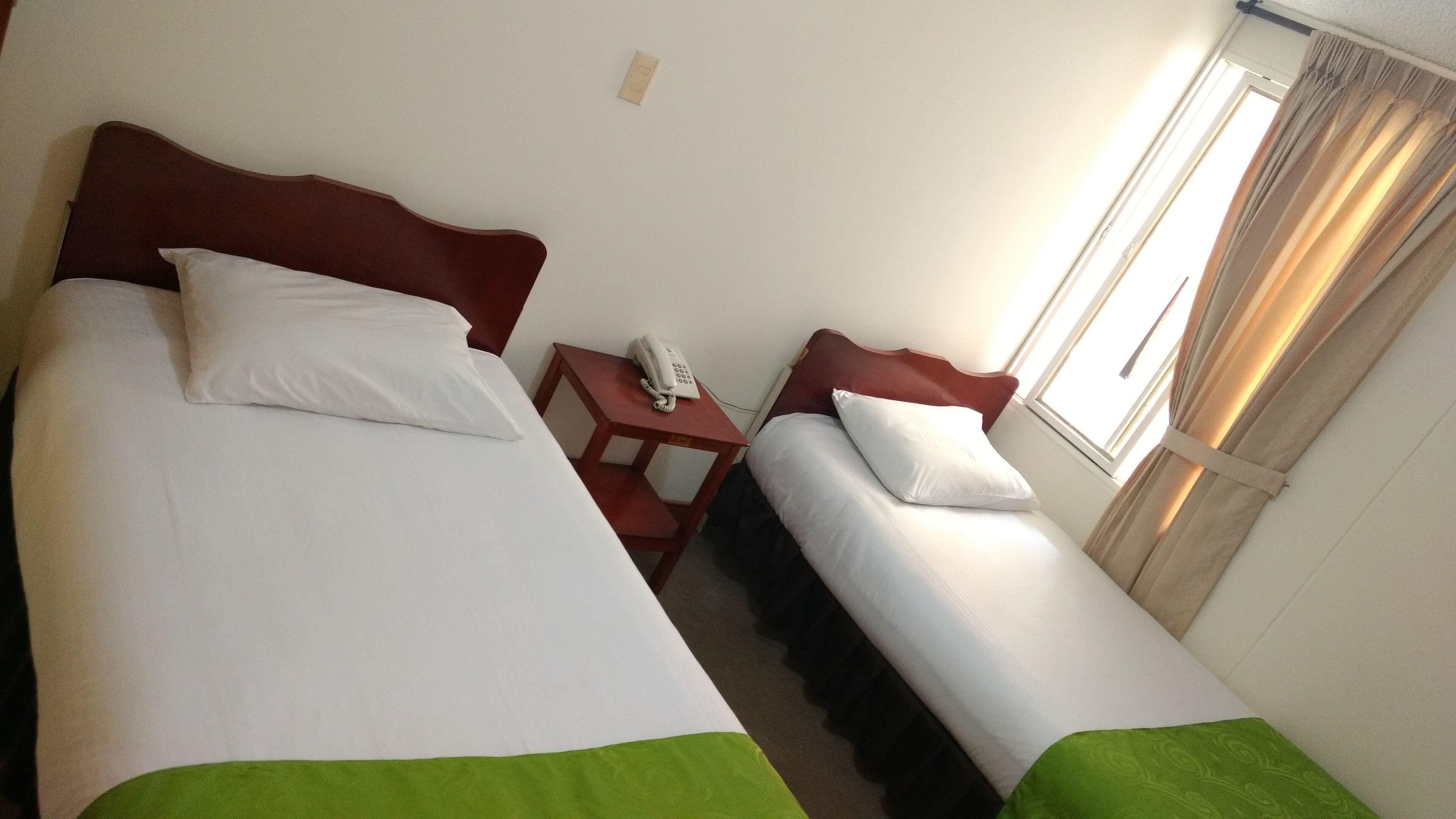 A hotel room with two beds, a bedside table with a phone, and a window with curtains.