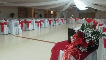 A large hall with rows of tables covered in white tablecloths and red sashes, likely set up for an event.