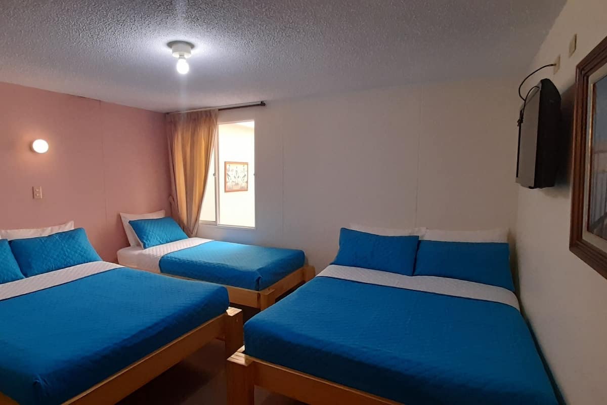 Una habitación con tres camas, cada una con ropa de cama azul, un escritorio de madera, un teléfono y un cuadro en la pared.