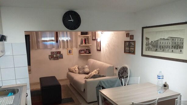 A living room with a sofa, a dining table with chairs, a clock, and a water bottle. - Open space apartment (Cecina)