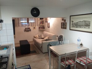 Un salon avec un canapé, une table à manger et des chaises, une horloge et une bouteille d’eau.