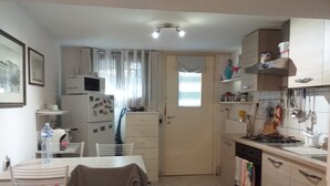 A compact kitchen with a refrigerator, microwave, and stove. There is a dining area with a table and chairs. - Open space apartment (Cecina)