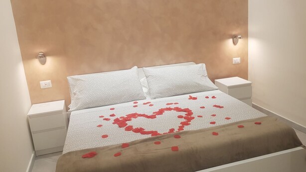 A neatly made bed with a heart-shaped arrangement of rose petals on the bedspread.