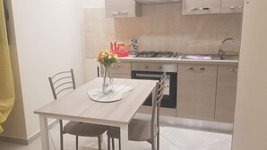 A compact kitchen with a dining table, chairs, a vase with flowers, and a yellow curtain.