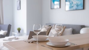 Une table à manger avec deux bols et deux verres à vin, placée dans un salon moderne avec un canapé et une petite table d’appoint.