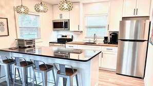A modern kitchen with a central island, bar stools, stainless steel appliances, and pendant lighting. - 122 Falkirk Small Pet Friendly Cottage near Beach (Fort Myers Beach)
