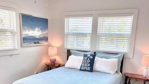 A bedroom with a bed, two windows, a ceiling fan, and a painting on the wall. - 122 Falkirk Small Pet Friendly Cottage near Beach (Fort Myers Beach)