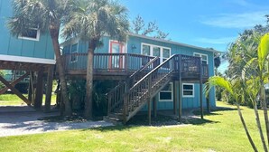 A two-story house with a balcony, wooden stairs, and palm trees. - 122 Falkirk Small Pet Friendly Cottage near Beach (Fort Myers Beach)
