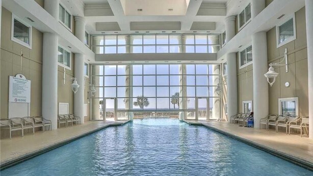 An indoor swimming pool with clear views through large windows, lounge chairs, and a sign on the wall. - Full Ocean Views, Steps to the Sand, Beach Chairs, Heated Pool/Hot Tub, Sleeps 8 (Miramar Beach)