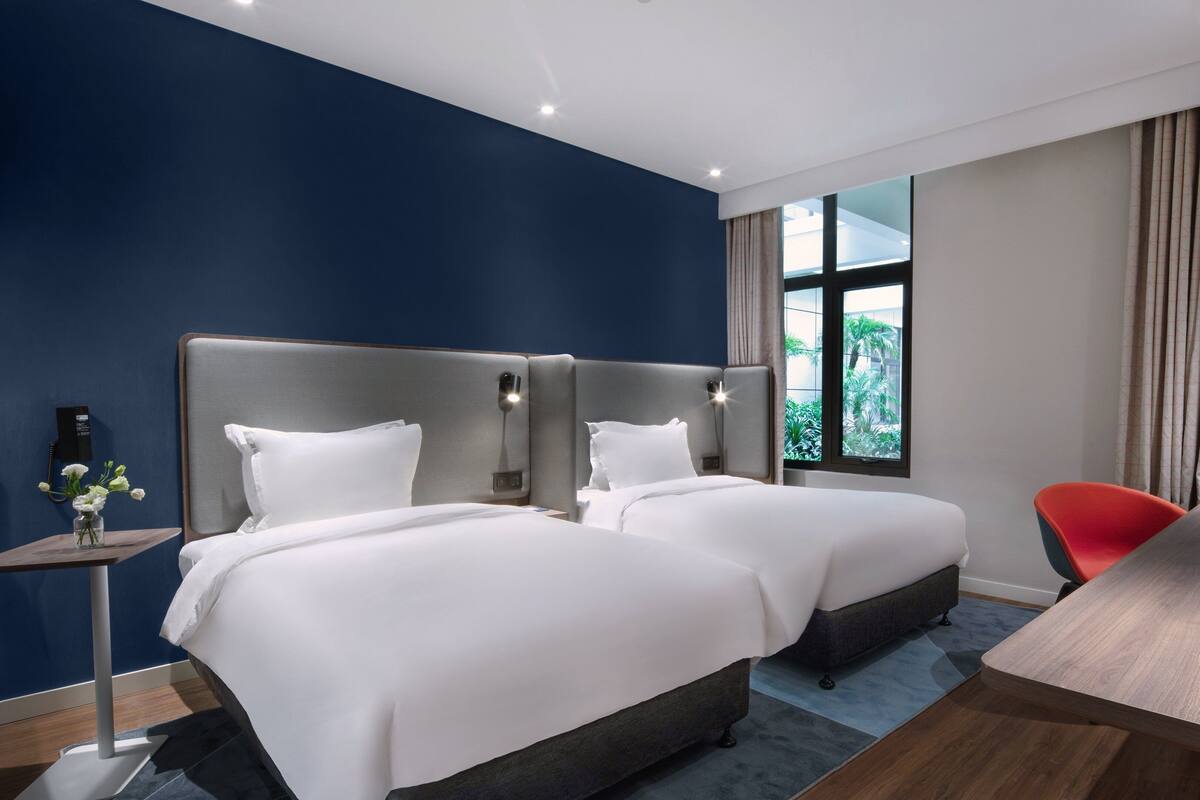 Une chambre d’hôtel avec deux lits, un bureau, une chaise, un téléphone et une fenêtre avec des rideaux.