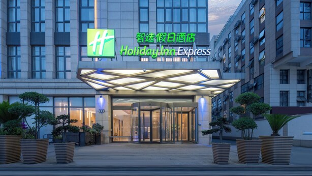 A Holiday Inn Express hotel entrance with a modern design, featuring a glass revolving door and potted plants.
