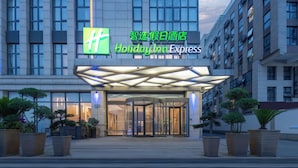 A Holiday Inn Express hotel entrance with a modern design, featuring a glass revolving door and potted plants.