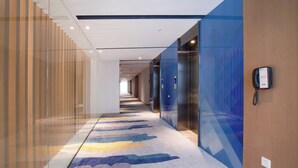 A modern hotel corridor with glass walls, a patterned carpet, and a phone on the wall.