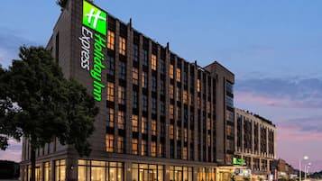 En moderne hotelbygning med et markant grønt skilt, flere etager og en godt oplyst indgang.