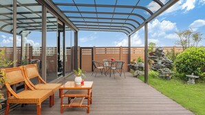 A covered outdoor area with a wooden deck, wicker furniture, and a glass enclosure.