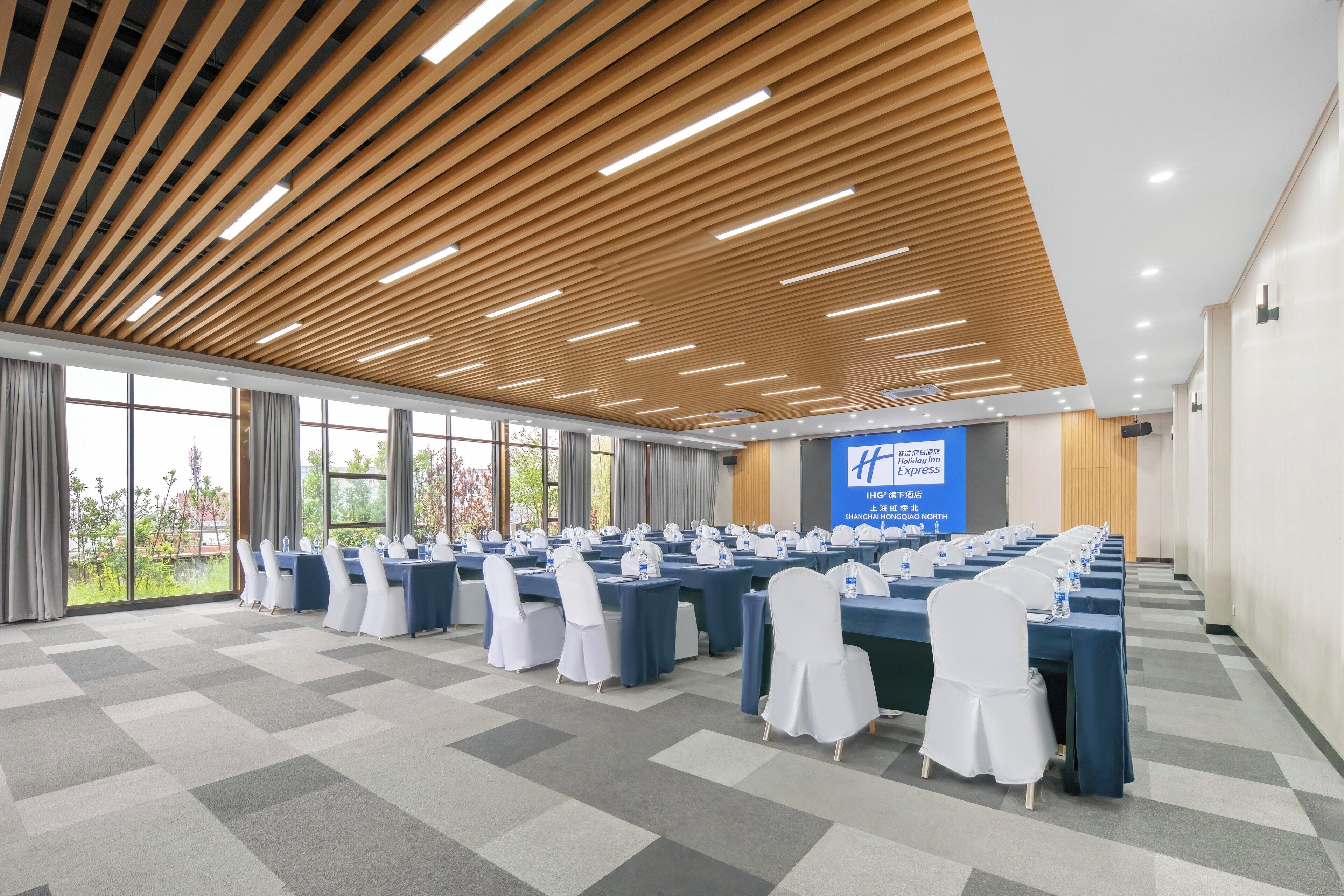 Un salón de conferencias con mesas largas, sillas blancas y una pantalla grande.