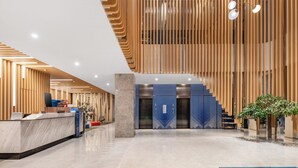 A modern hotel lobby with a reception desk, elevators, and a staircase.
