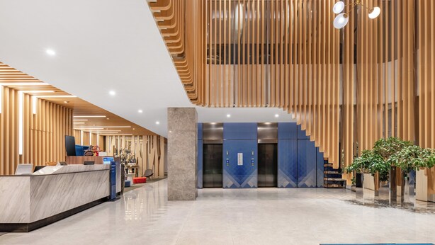 A modern hotel lobby with a reception desk, elevators, and a staircase.