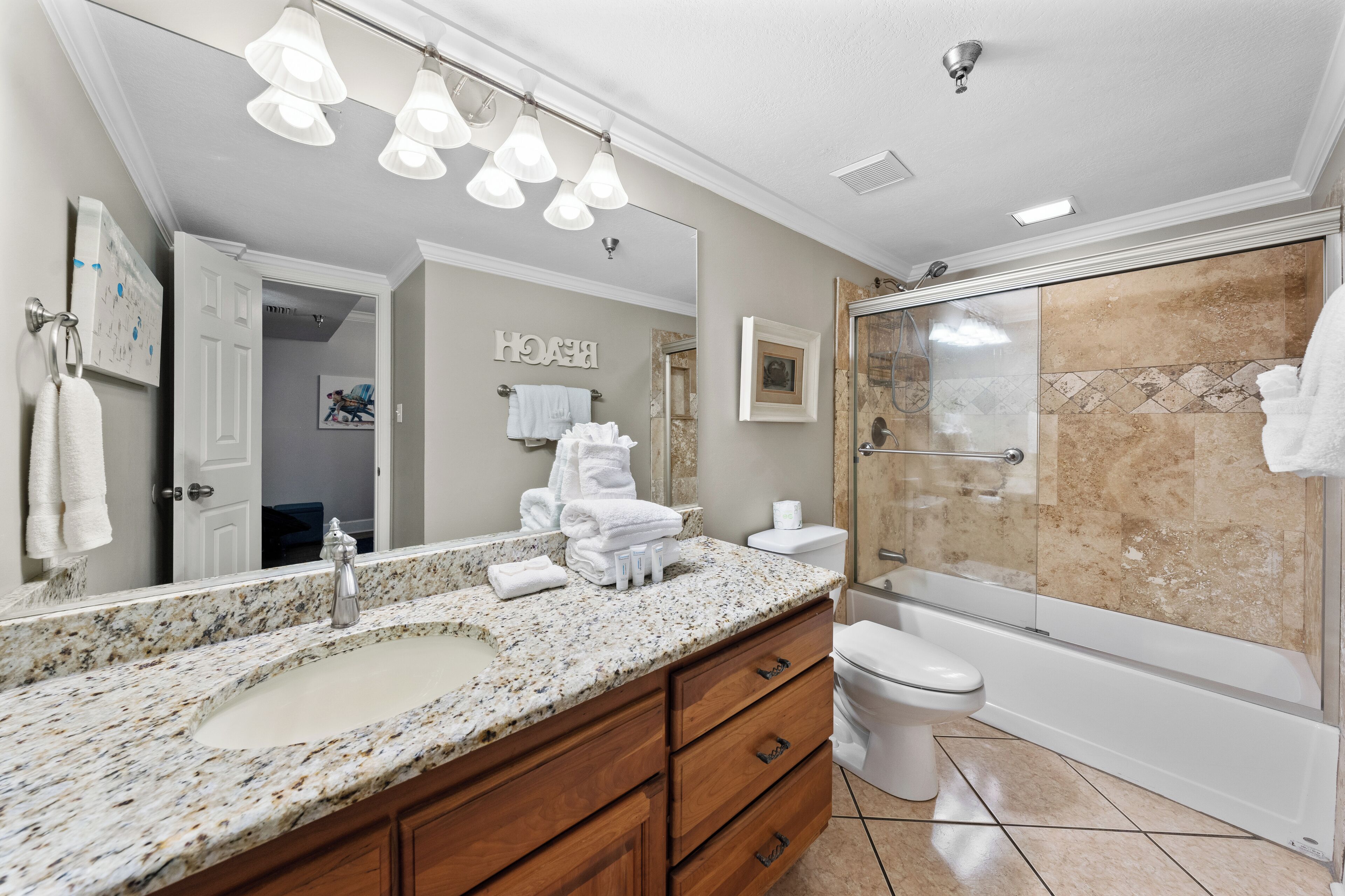 A bathroom with a granite countertop sink, wooden vanity, a large mirror, and a glass-enclosed shower.