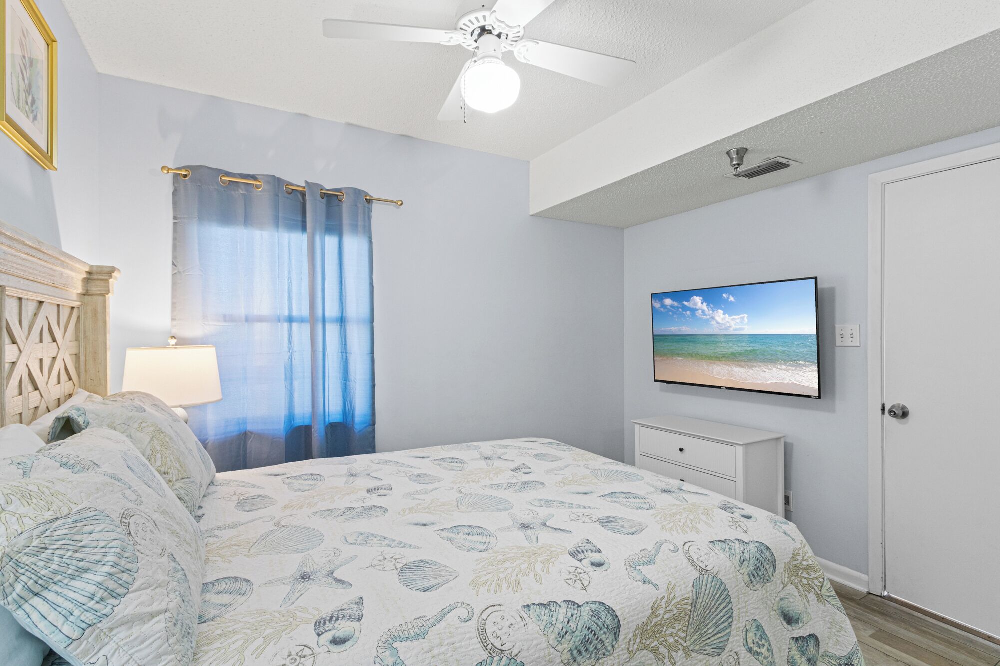 A bedroom with a bed, a ceiling fan, a TV on the wall, and a window with curtains.