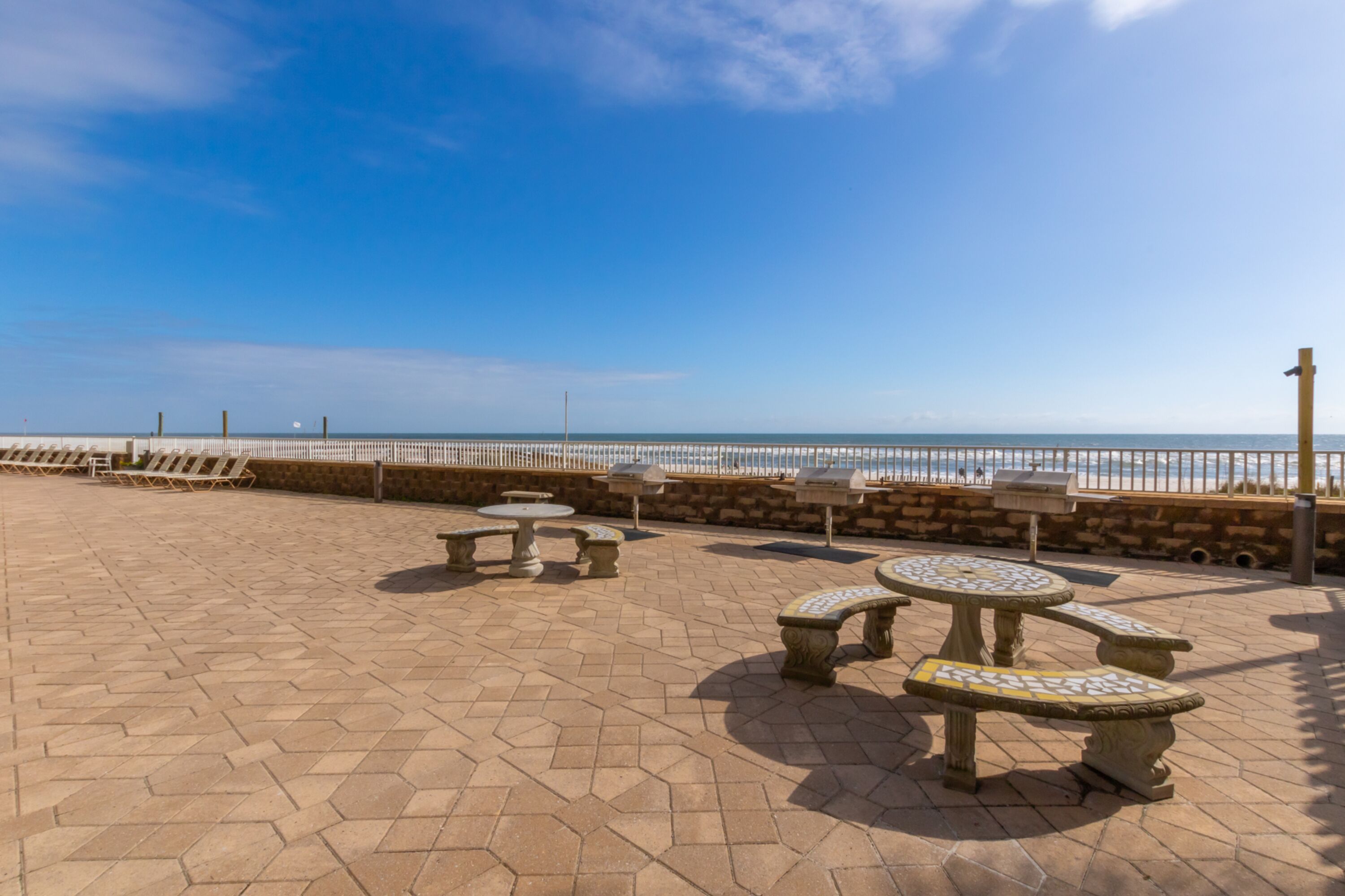 An outdoor patio with hexagonal stone tiles, several stone tables and benches, and a view of the ocean.