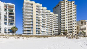Un hôtel en bord de mer, avec plusieurs étages, des balcons et une plage de sable au premier plan.