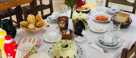 A dining table set with various dishes, including bread, pastries, and a cake, along with condiments and drinks.