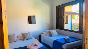 Una habitación con dos camas, cada una con cubrecama y almohadas azules, y un ventanal con vistas al exterior.