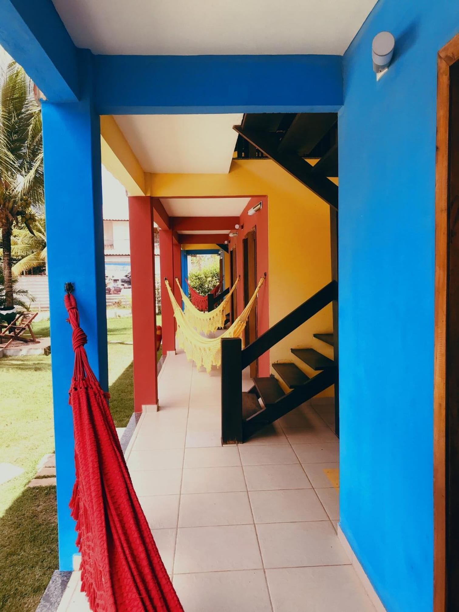 A bright hallway with blue and yellow walls, a red hammock, and a staircase.