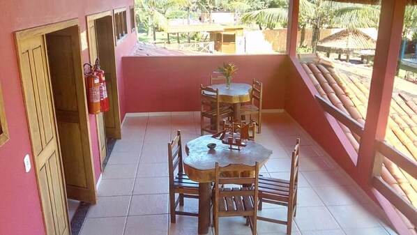 A covered outdoor area with a wooden table and chairs, a fire extinguisher, and a view of the surrounding area. - Pousada Pérola da Barra (Maraú)